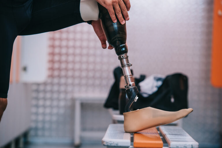 cropped shot of sportsman putting on his artificial leg at changing room of gym