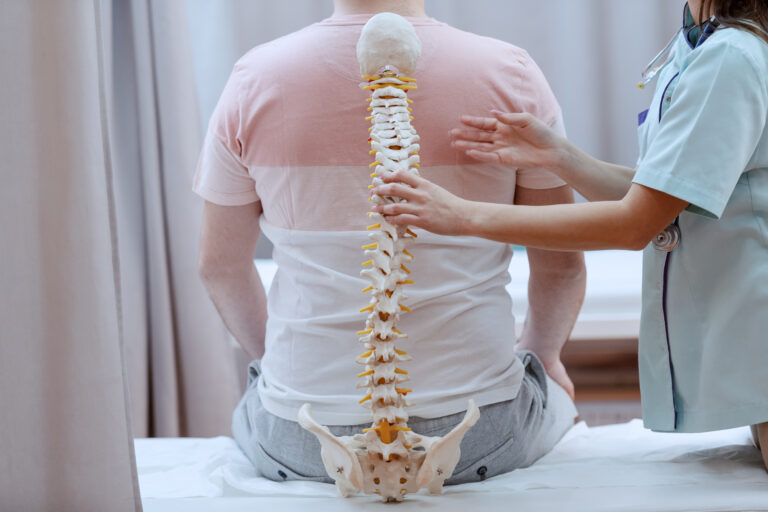 Caucasian nurse holding spine model against the patients backs. Clinic interior.