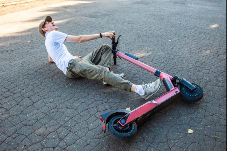 A young man got into an accident on an electronic scooter, lies on the asphalt and screams in pain