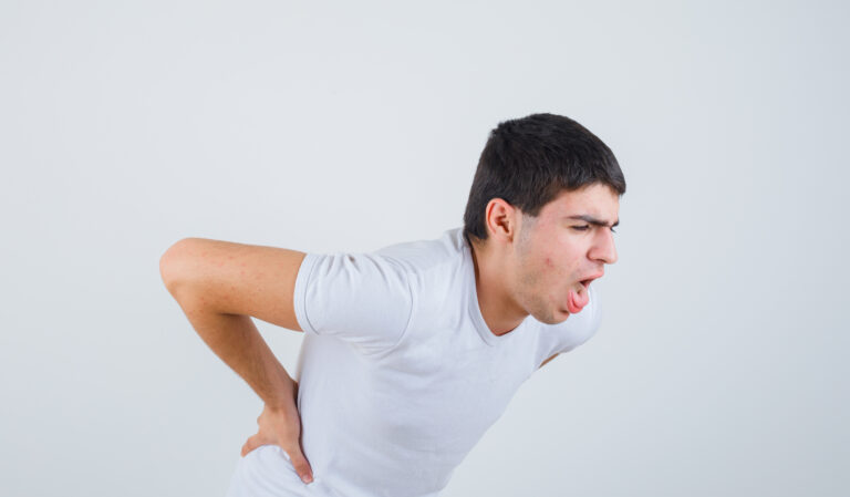 young male in t-shirt suffering from lower back pain and looking unwell , front view.